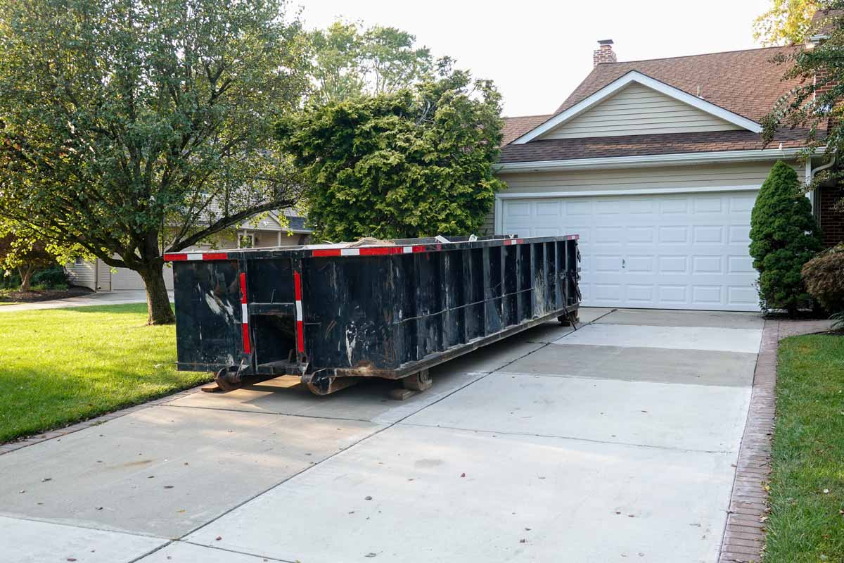 A black dumpster sitting in a beige home's driveway